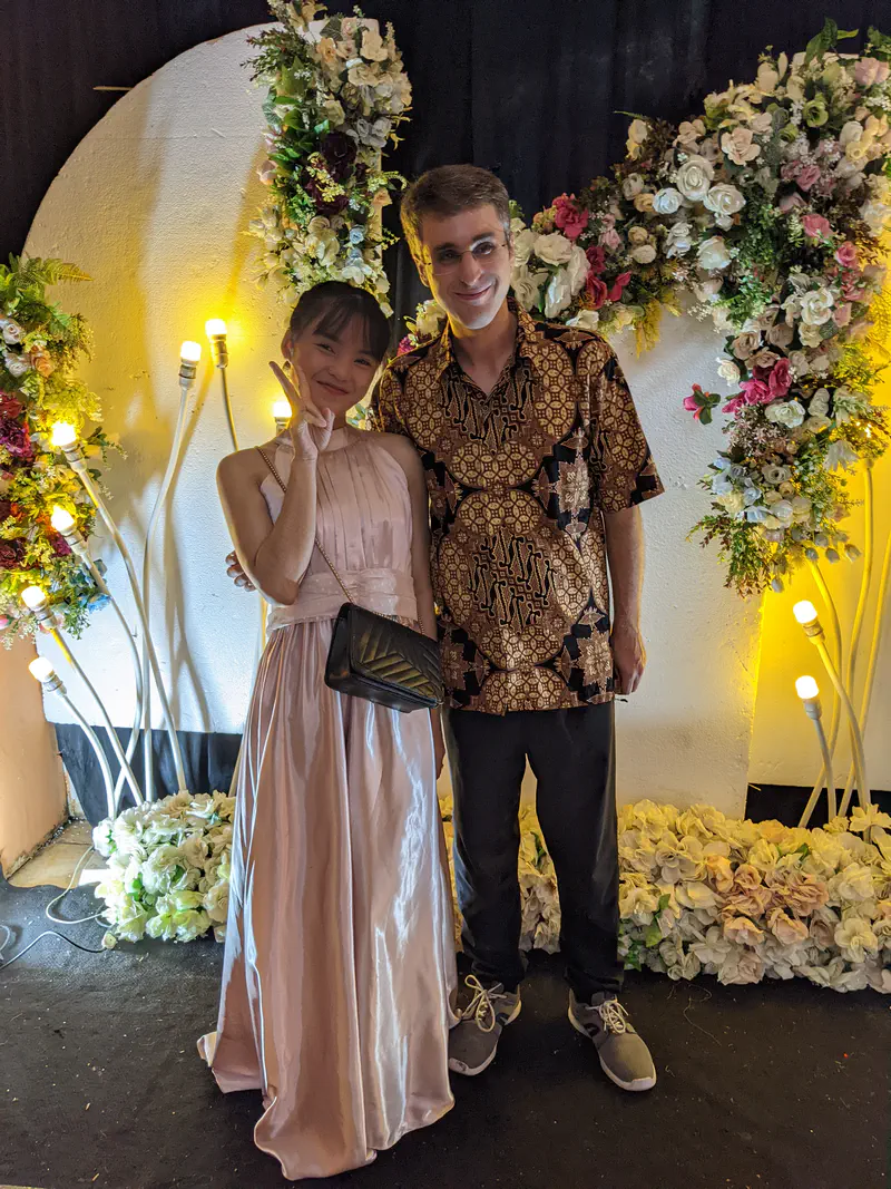 Two people dressed formally posing in front of a floral backdrop.