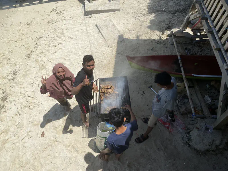Group of people grilling food on a barbecue at the beach.