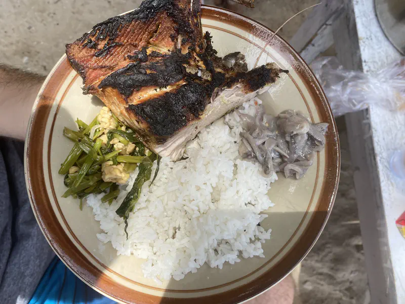 Plate of rice with grilled fish, sautéed greens, and a side of shellfish.
