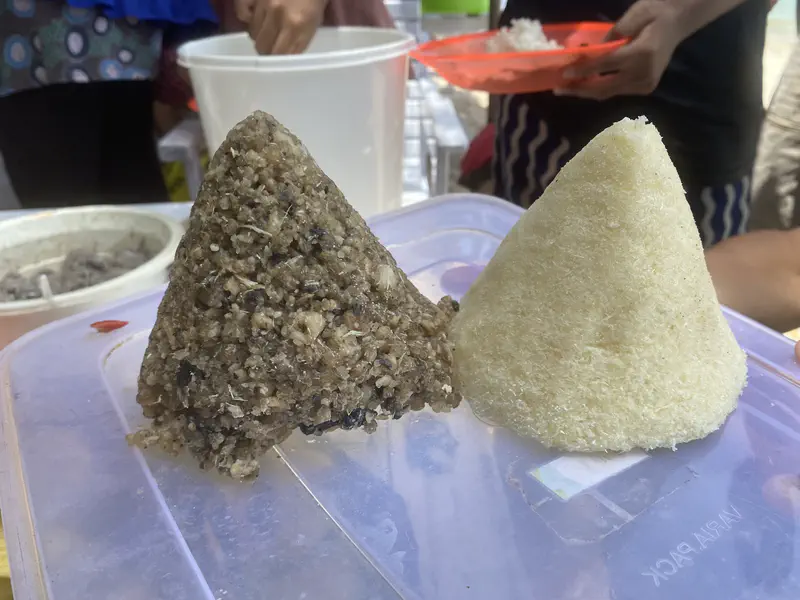 Two cone-shaped traditional foods, one dark and one light, placed on a container lid.