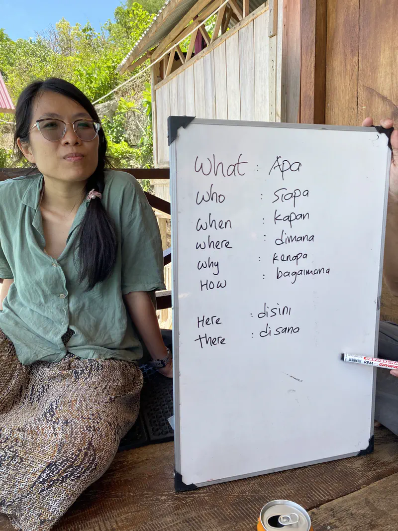 Person sitting next to a whiteboard showing English words with Indonesian translations.