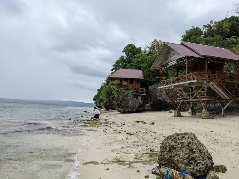 Wooden beach huts on stilts built on rocks by the shoreline.