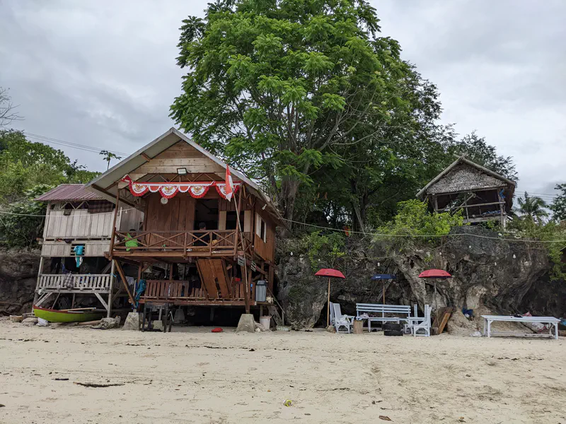 Wooden houses and small huts along a sandy beach with umbrellas and seating.