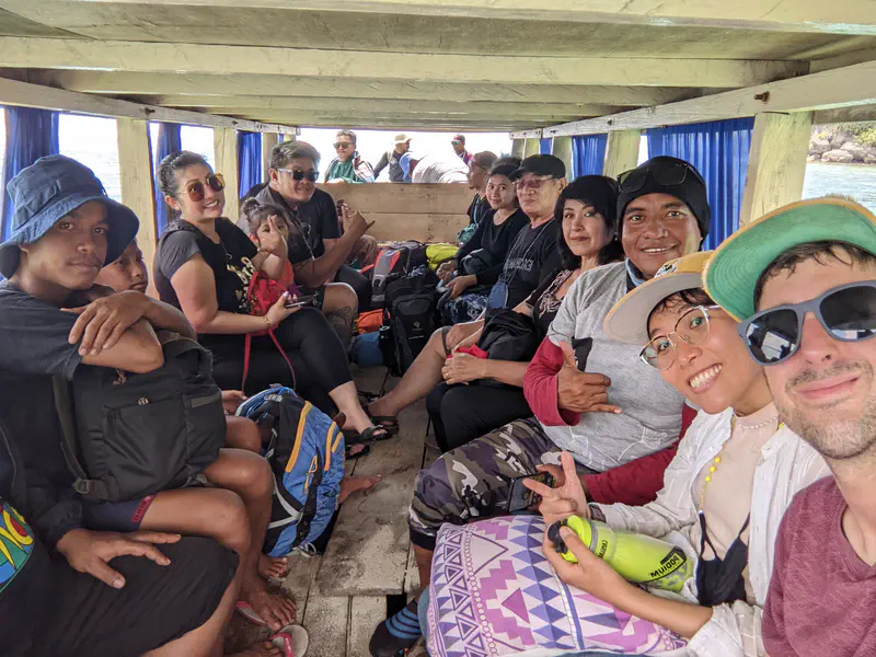 Group of people sitting closely together inside a wooden boat, smiling and posing for the camera while traveling on the water.