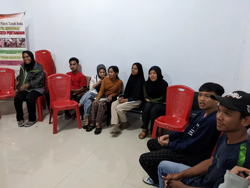 Group of teenagers sitting in a semicircle on red chairs indoors, listening and talking together.