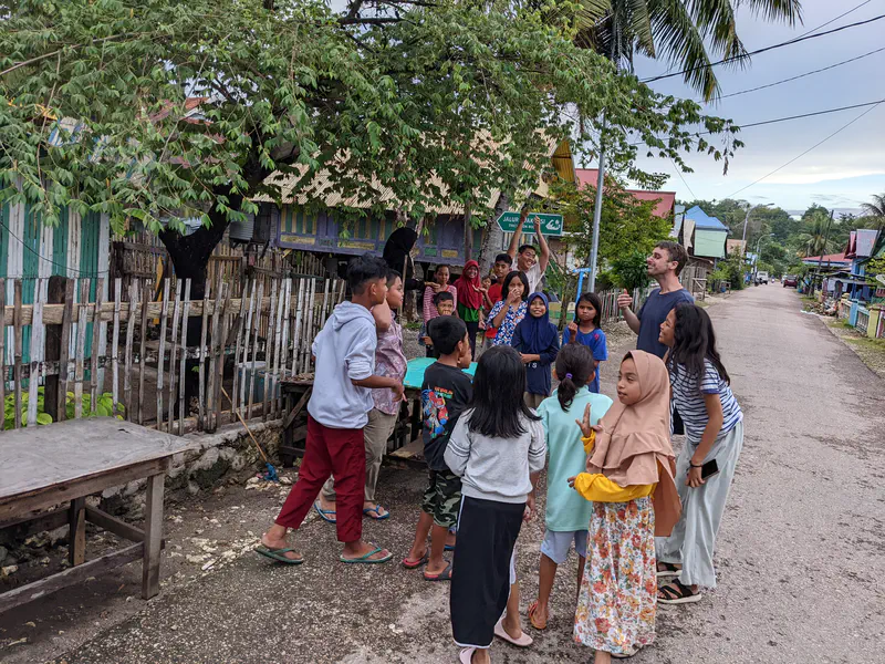Group of children and an adult gathered on a village street, engaging in a lively outdoor activity.