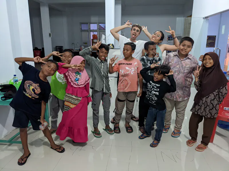 Children and two adults indoors making playful peace sign poses and smiling at the camera.