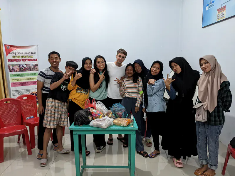 Group of teenagers and adults standing indoors behind a table with snacks, smiling and posing for a photo.