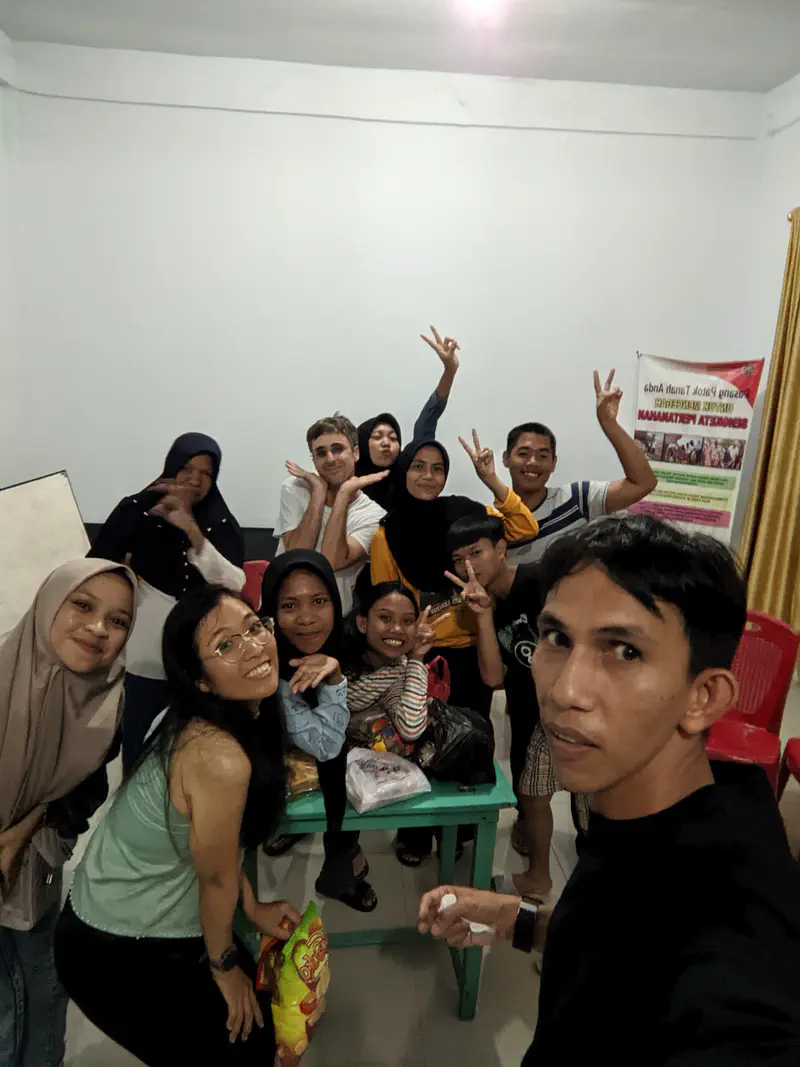 Group of teenagers and adults indoors smiling and making peace signs while posing for a selfie.