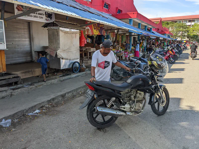 Man pushing a black motorcycle in front of a row of market stalls.