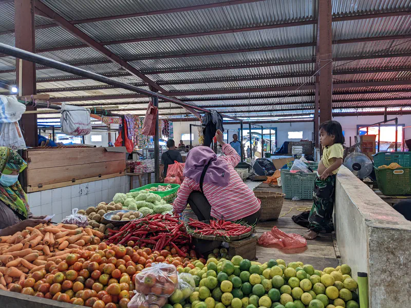 Vendors selling carrots, tomatoes, chilies, and limes at a vegetable stall in a market.