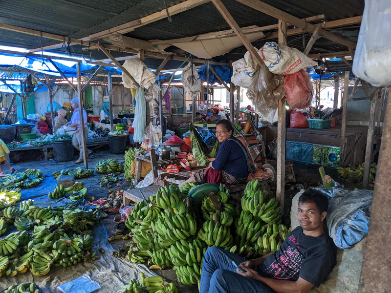 Vendors sitting among piles of green bananas at a busy covered market.
