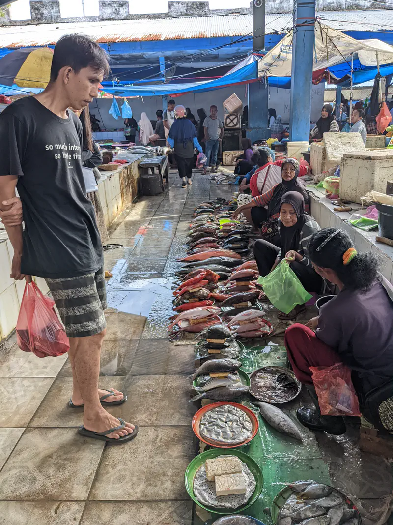 Man browsing rows of fresh fish and seafood sold by vendors on the floor at a market.