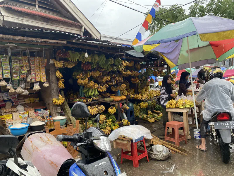 Banana stall at a rainy outdoor market with bunches of bananas hanging and stacked for sale.