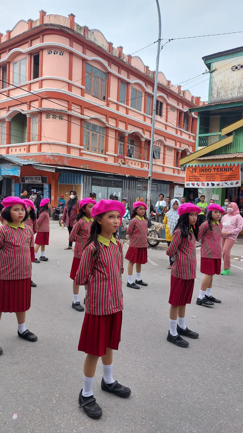 Girls in striped uniforms and pink berets standing in formation during a street parade.