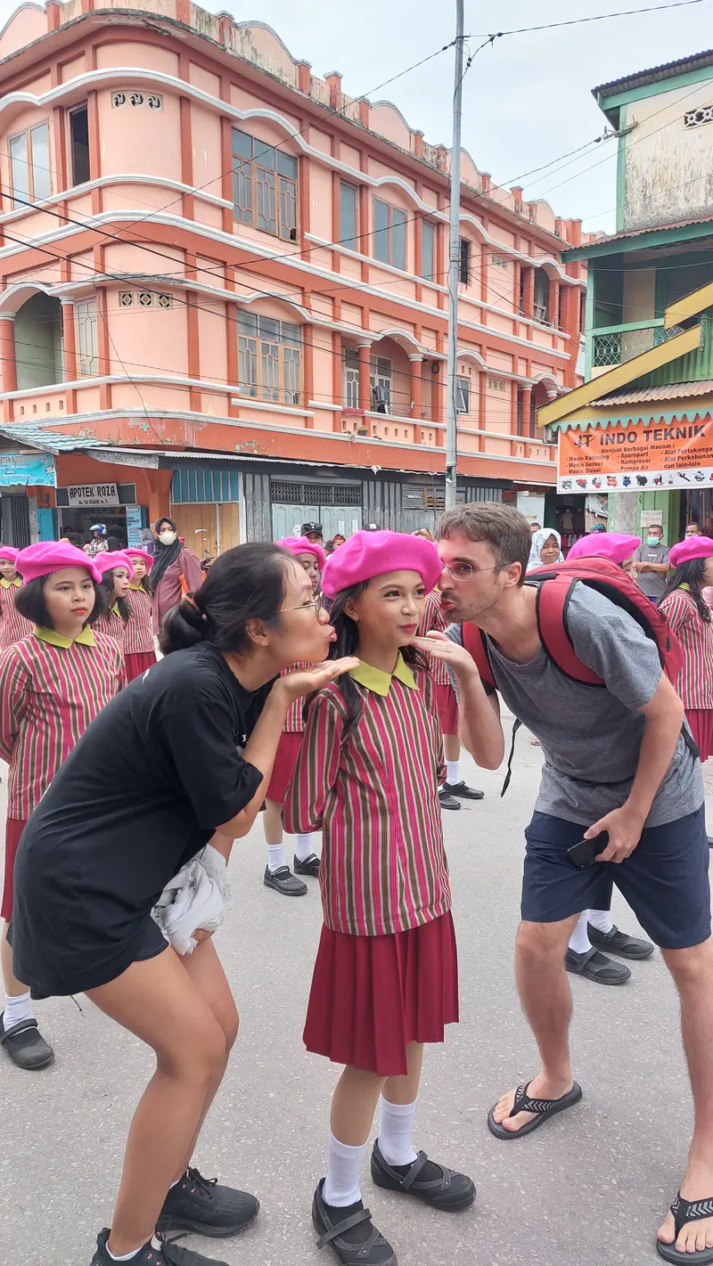 Two adults posing playfully with a girl in a striped uniform and pink beret during a street parade.