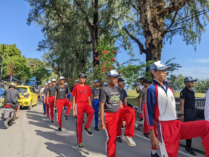Group of boys in sports uniforms marching in formation on a street.
