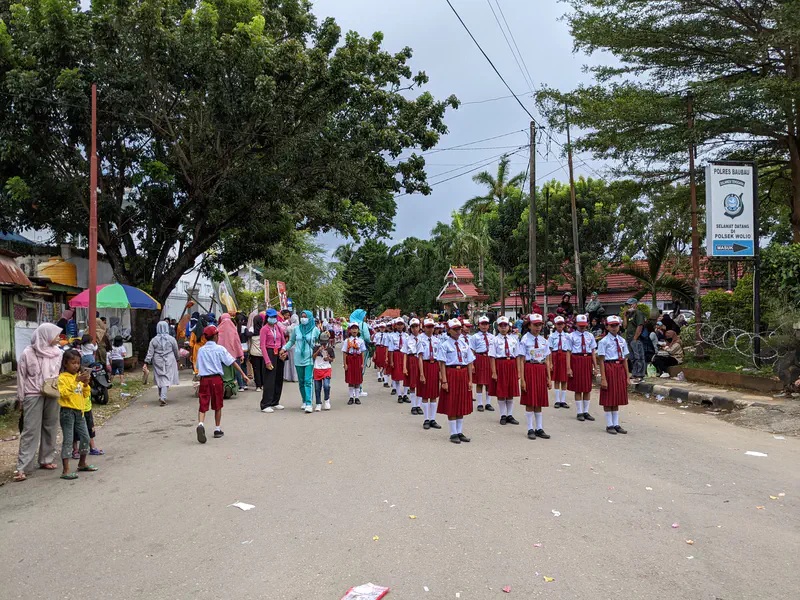 Group of elementary school students in red and white uniforms standing in formation during a street parade.