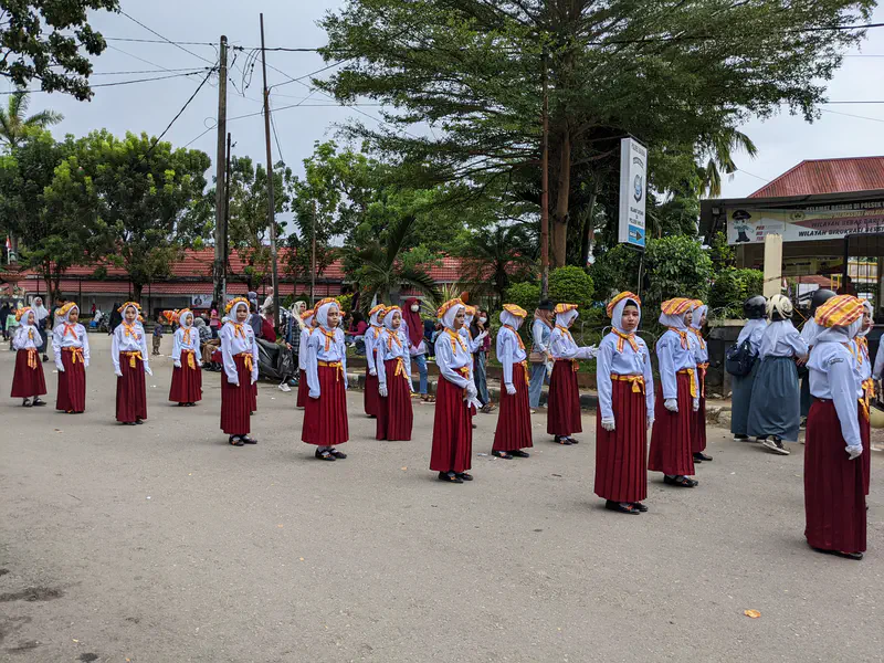 Girls in red skirts and headscarves with yellow sashes standing in formation during a parade.