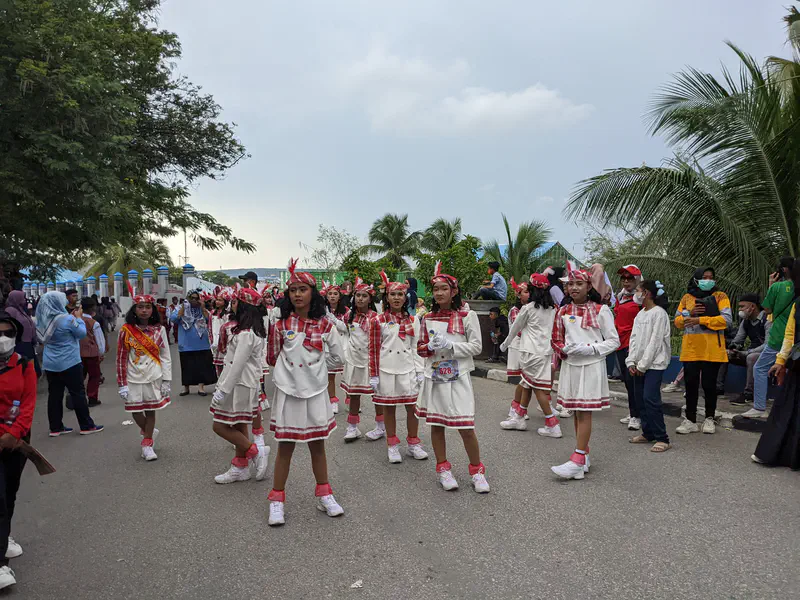 Girls in white and red costumes with feathered headbands preparing to march in a parade.