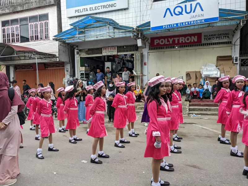 Girls in bright pink uniforms and berets standing in formation during a parade.