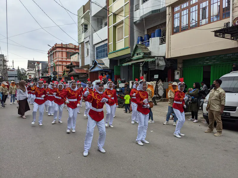 Marching band in red and white uniforms performing in a street parade.