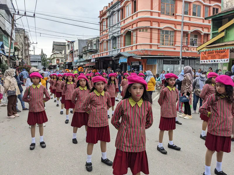 Group of girls in striped uniforms and pink berets marching in a street parade.
