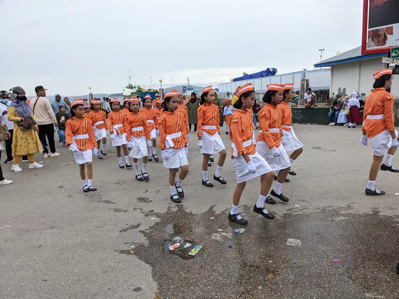 Girls in orange and white uniforms marching in formation during a parade.