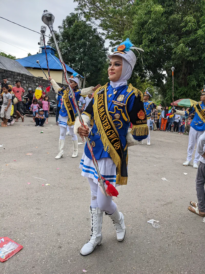 Female drum major in blue uniform and tall white boots leading a marching band.
