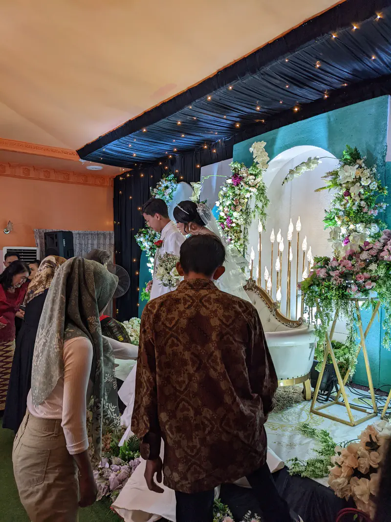 Guests greeting the bride and groom on stage during a wedding ceremony with floral decorations.