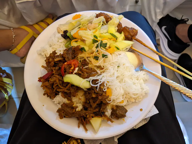 Plate of food with rice, noodles, vegetables, beef, and satay skewers served at a wedding reception.
