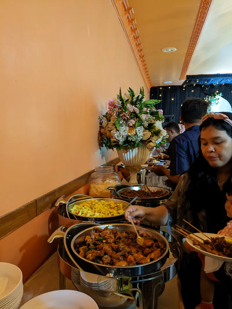 Guests serving themselves from a buffet with Indonesian dishes at a wedding reception.