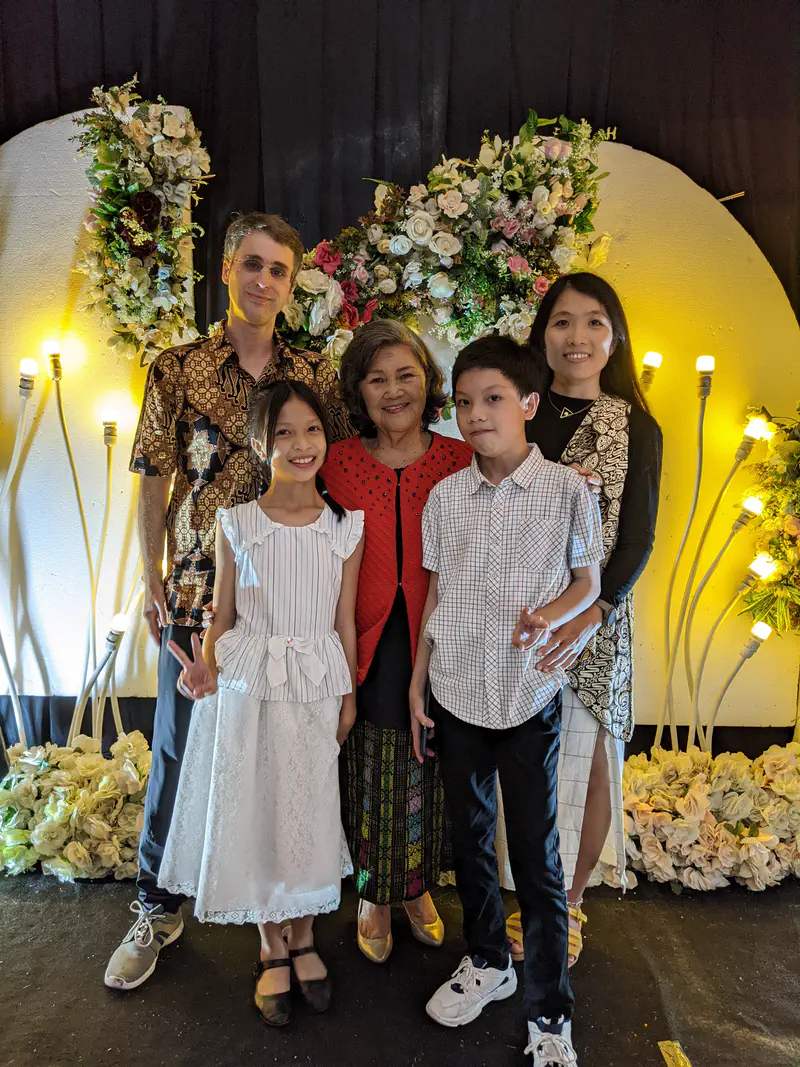 Family group photo with floral wedding backdrop, including adults and children smiling together.