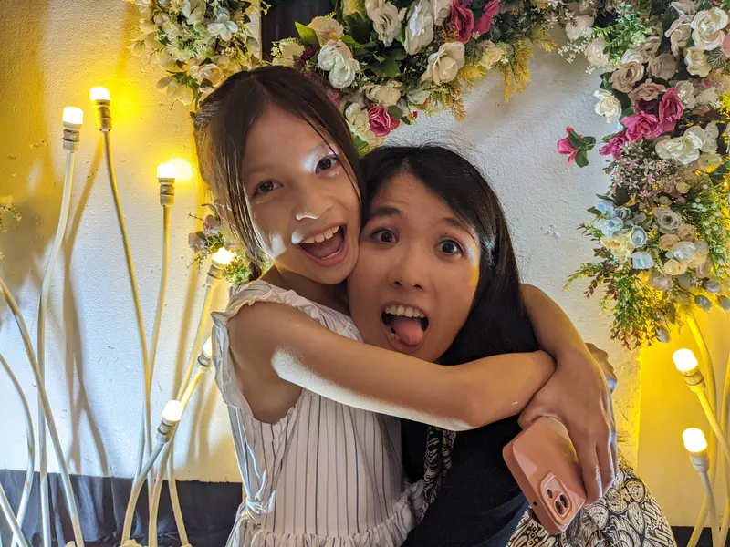 Young girl hugging a woman playfully while posing in front of a wedding floral backdrop.