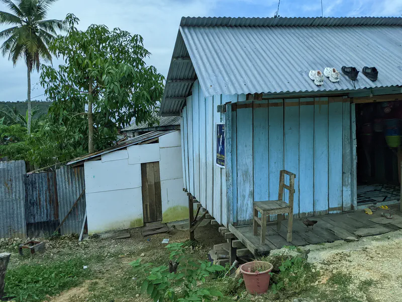 Small wooden house with a corrugated metal roof, a wooden chair on the porch, and shoes placed on the roof.