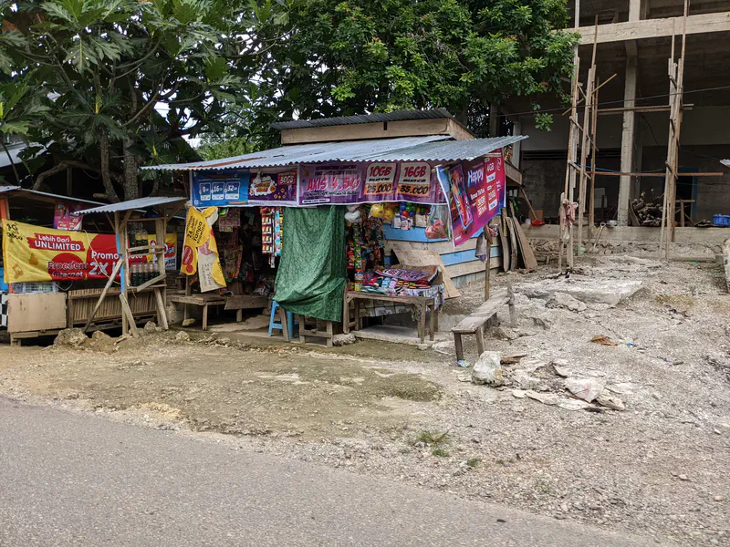 Small roadside kiosk selling snacks and goods with colorful banners and tarps.