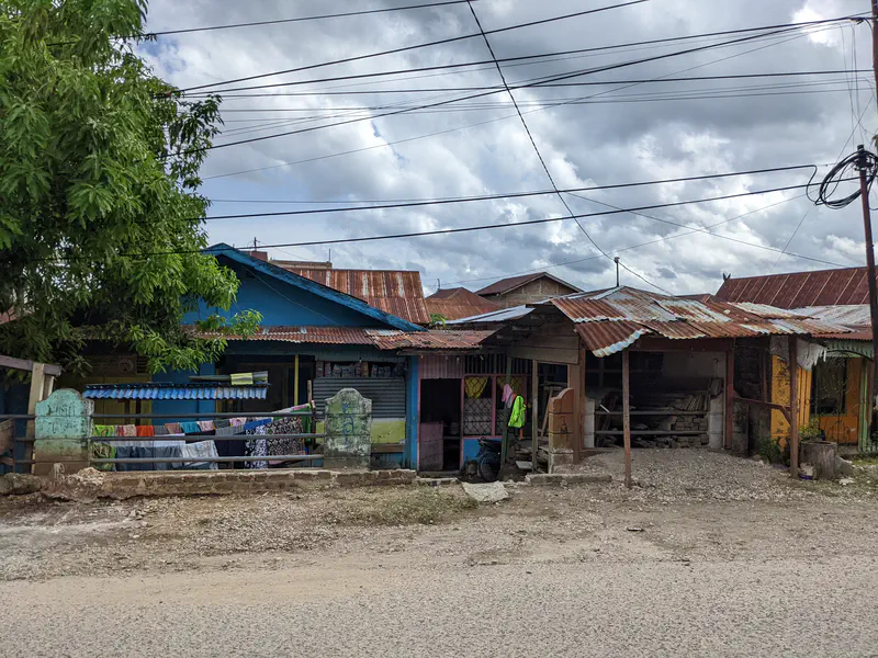 Row of small houses with rusted tin roofs and laundry hanging outside along a village road.