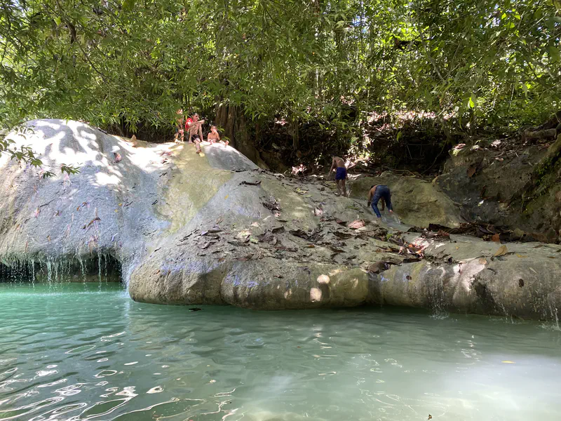Children climbing and sitting on rocks above a turquoise pool beside a small waterfall.