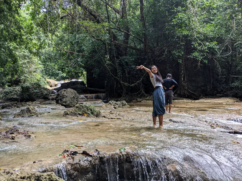 Woman smiling and posing in a rocky forest stream while another person stands nearby.