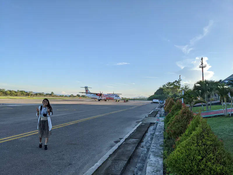 A person walking on the airport tarmac with a Wings Air propeller plane in the background.