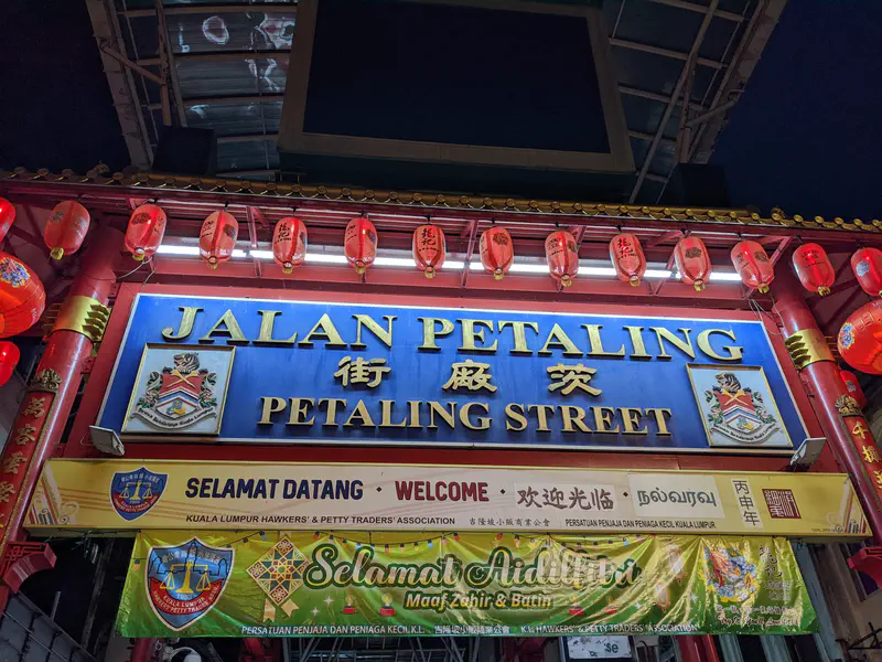 Entrance sign for Petaling Street in Kuala Lumpur, decorated with red lanterns and banners welcoming visitors in multiple languages.
