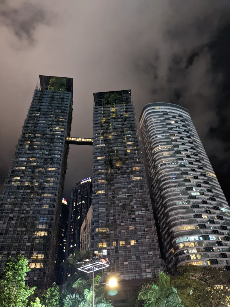 Tall modern skyscrapers at night with a cloudy sky, one building featuring a skybridge between two towers.