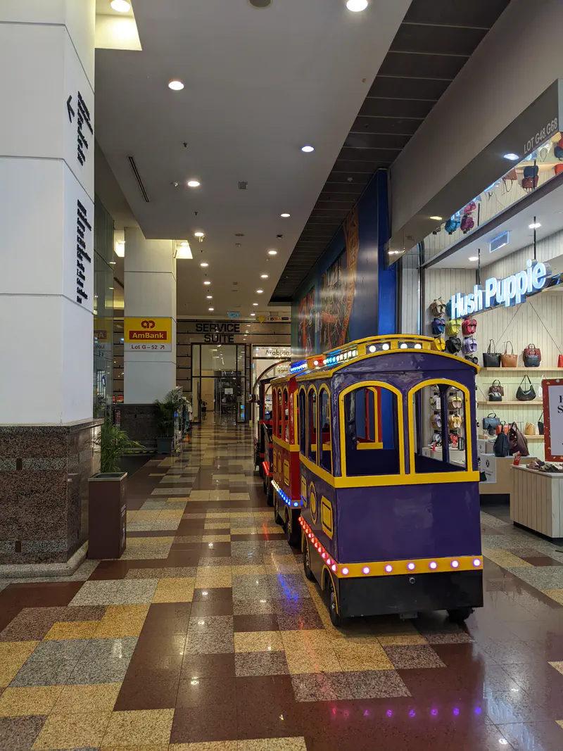 Miniature colorful train ride parked inside a shopping mall corridor with tiled floors and shops on both sides.