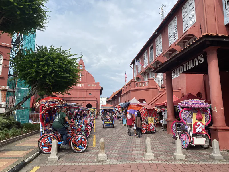 Colorful trishaws and tourists in front of Christ Church and Stadthuys in Melaka.