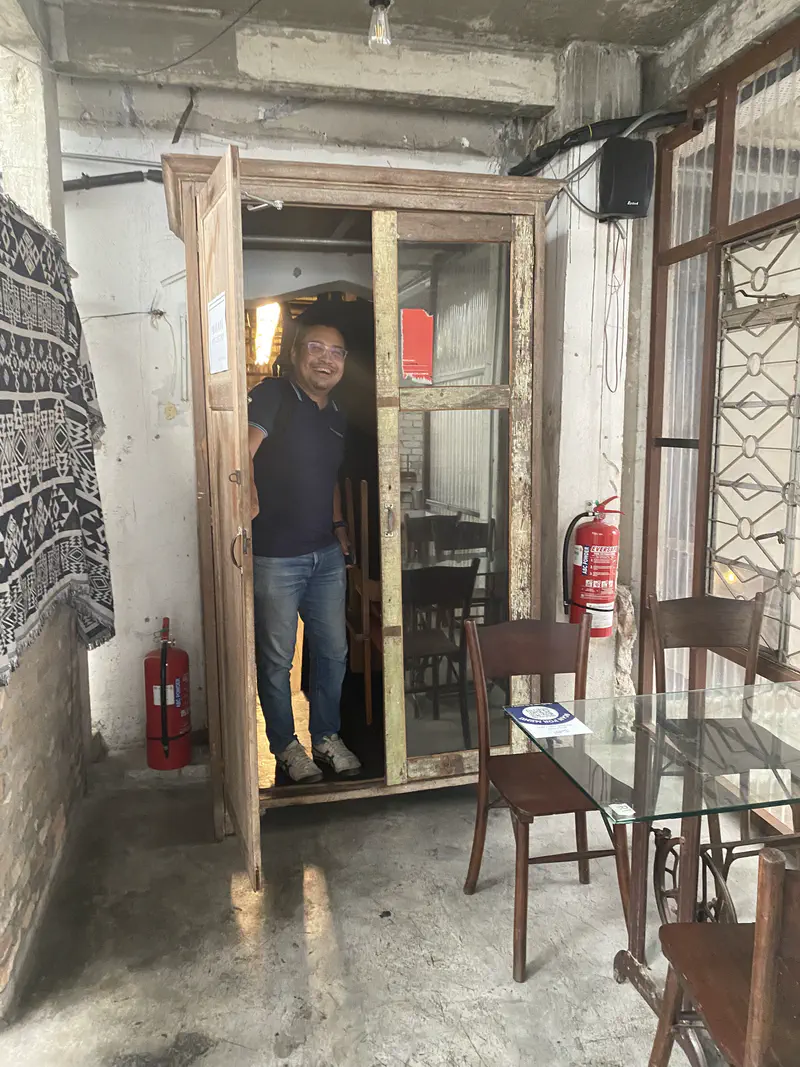 Man smiling while standing in the doorway of a rustic wooden booth in a café.