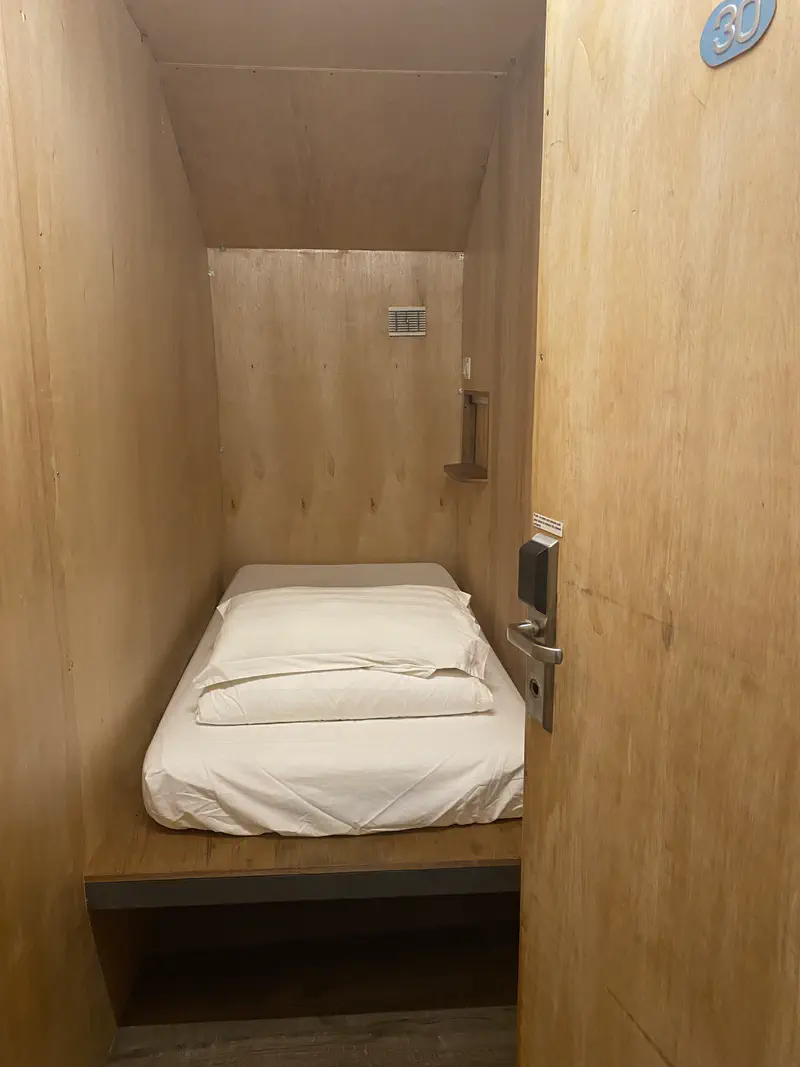 Small wooden room with a single bed, white bedding, and a door labeled 30.