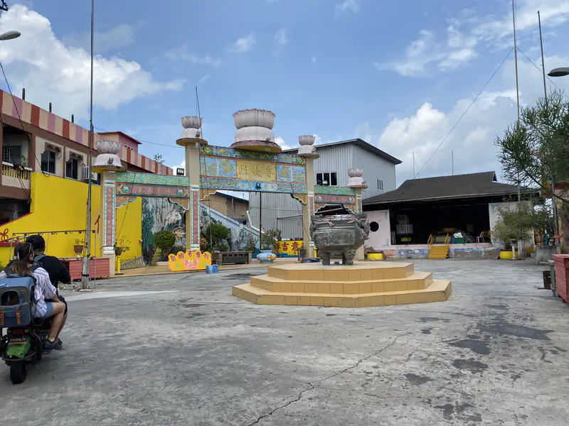 Colorful temple courtyard with a large incense burner on a pedestal and an ornate entrance gate decorated with lotus designs.