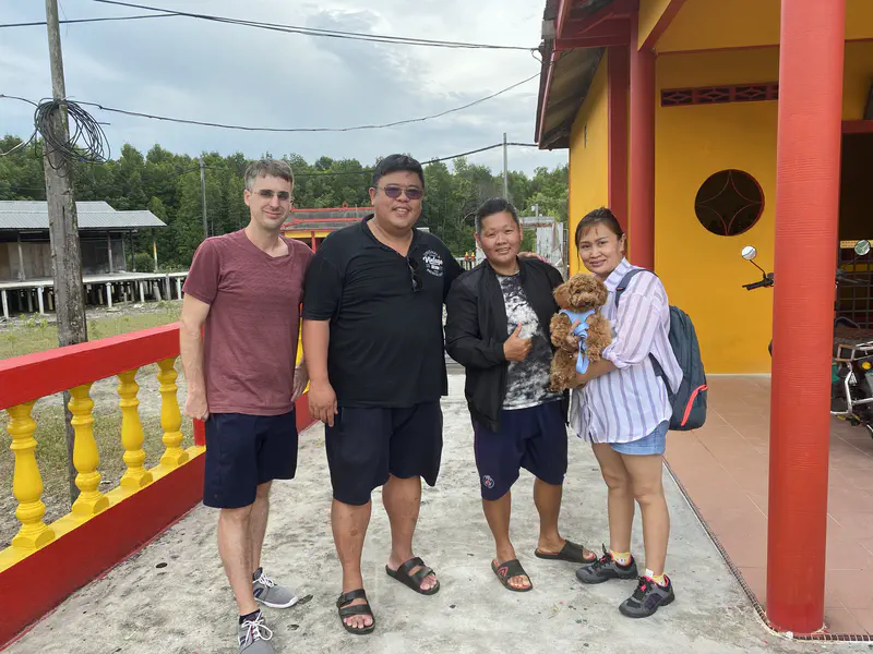 Four people posing together outside a bright yellow and red building, one of them holding a small brown dog.