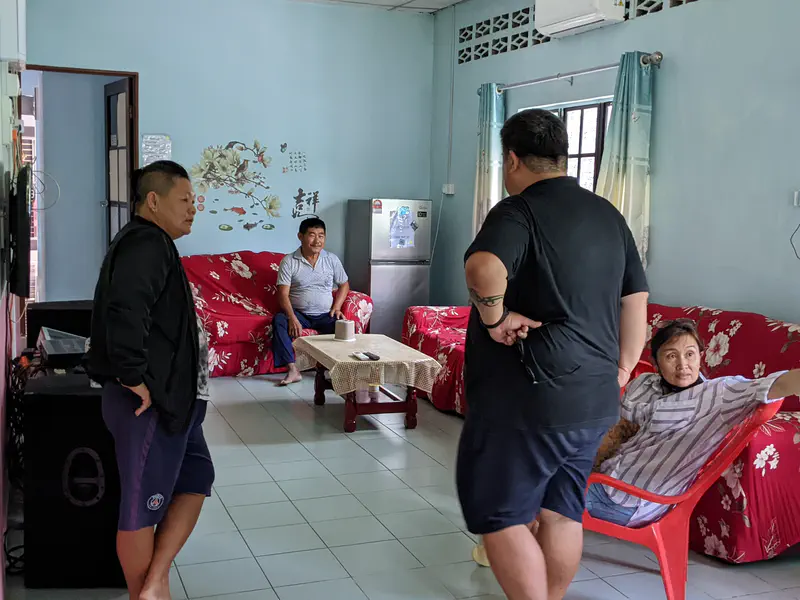 Four people gathered in a living room with red floral-patterned sofas and a light blue wall with decorative stickers.