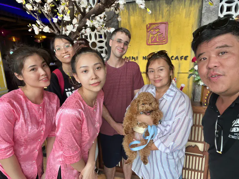 Group of people posing together in front of the Mini Nguyen Café entrance, with one person holding a small brown dog.